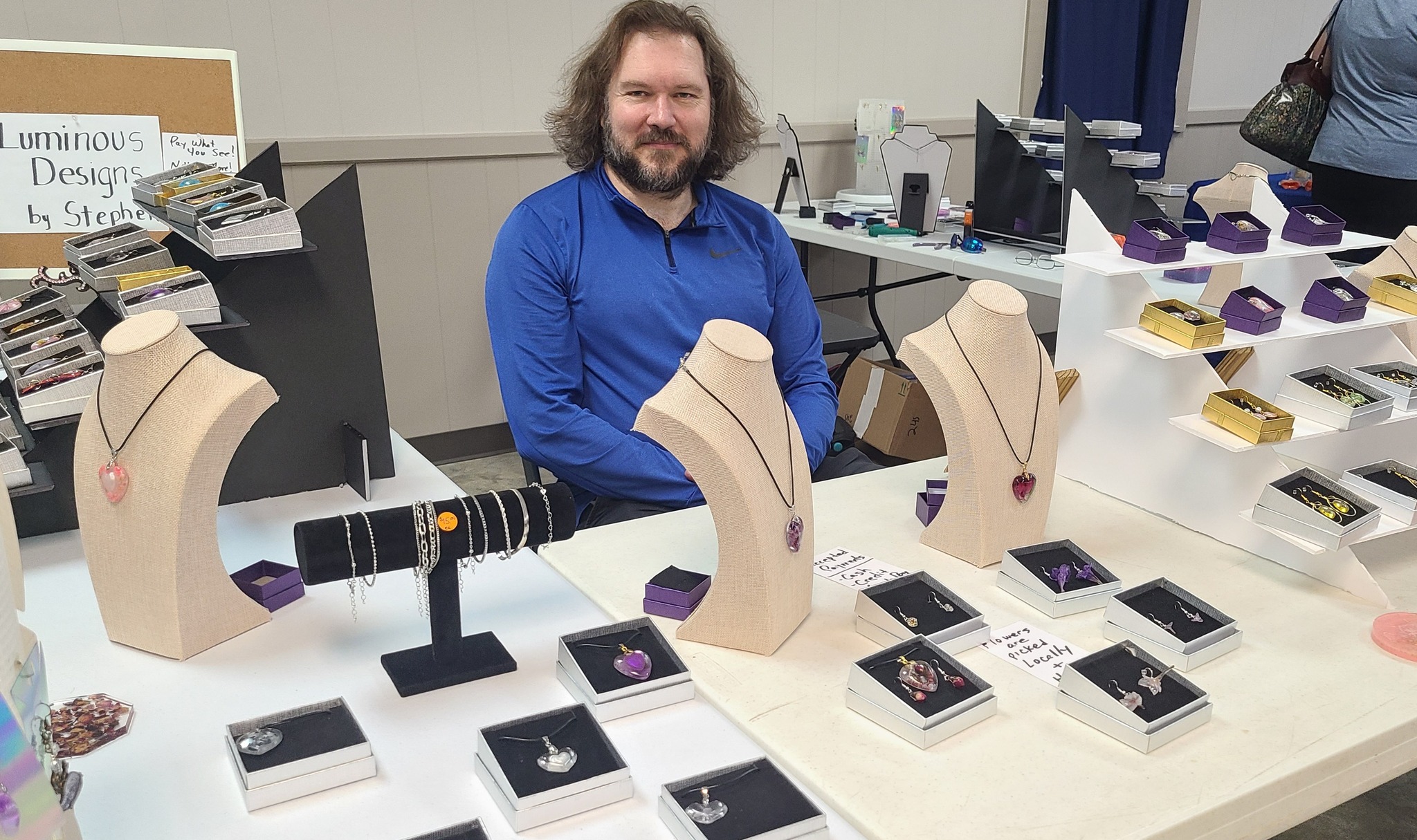 Stephen seated behind a display of Luminous Designs jewelry at a local market